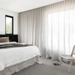 Minimalist-bedroom-with-white-bedding-black-headboard-cane-chair-and-floor-to-ceiling-linen-sheer-curtains
